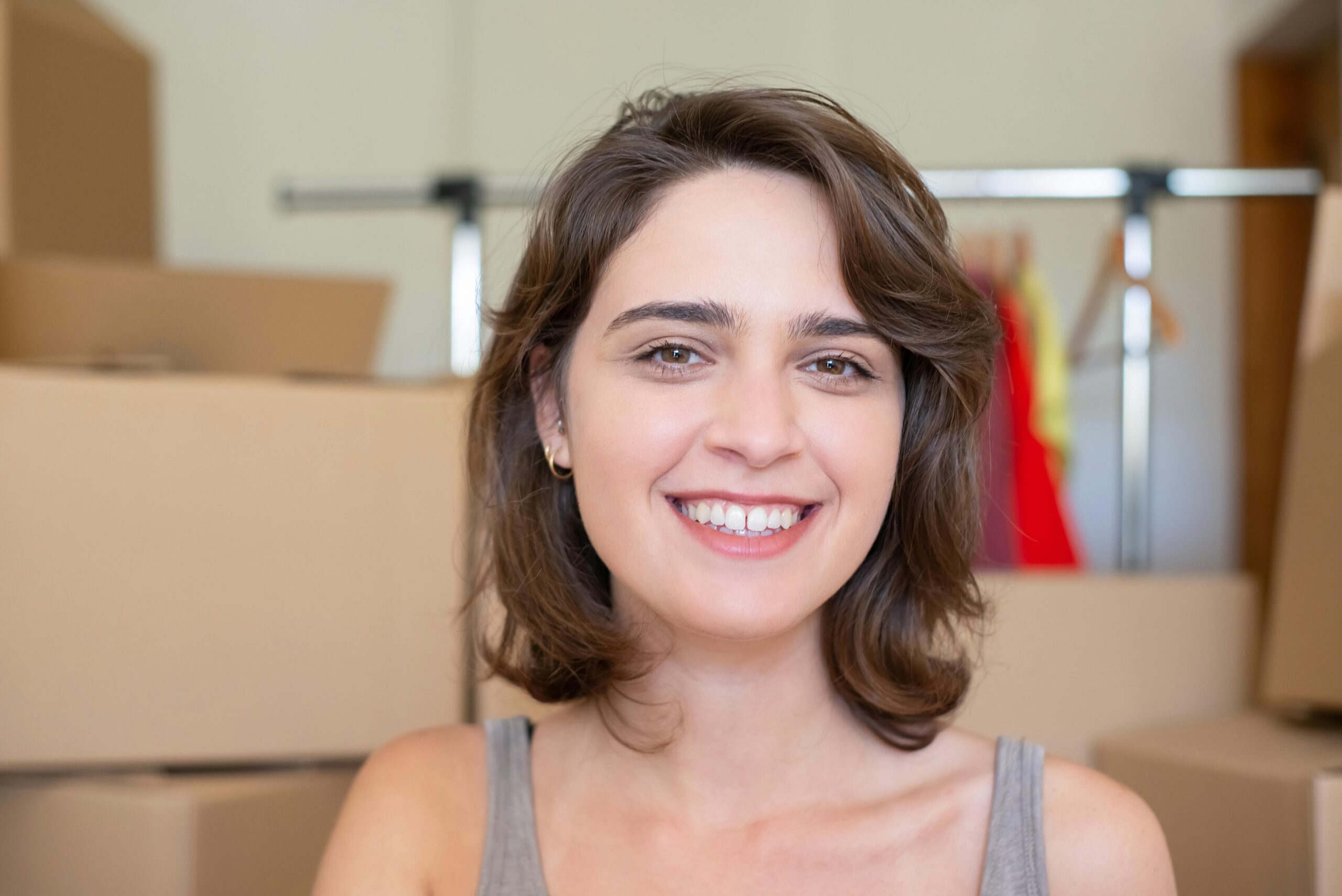 A happy woman with short brown hair smiling in a room with moving boxes, indoors.
