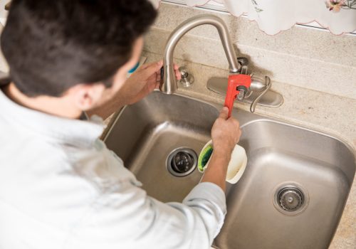 Male plumber using a wrench to tighten a water faucet in a kitchen, seen up close